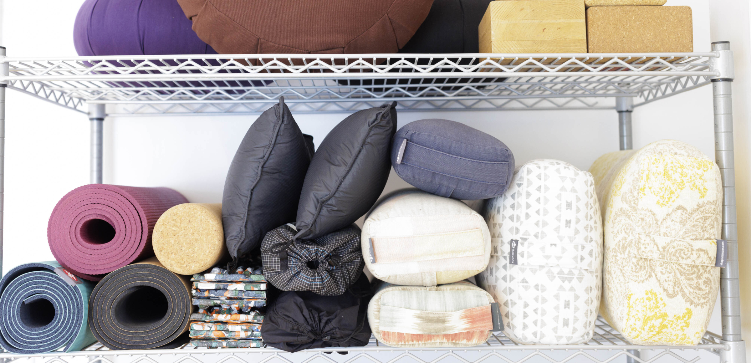 Somatic props on shelf: heart pillow, selection of bolsters, yoga mats, wood and cork blocks, curiosities.