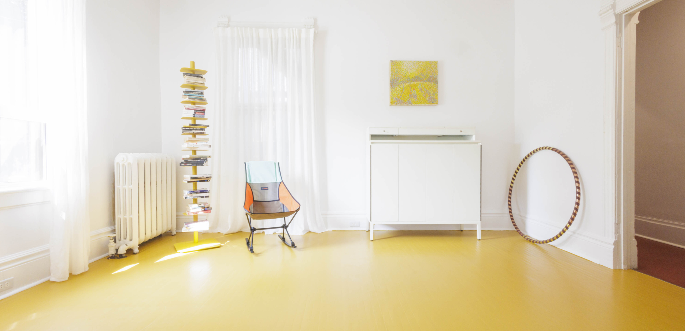 The Sensory Studio: sun drenched, expansive, soaring ceiling, yellow floor, white walls, colourful rocking chair, hula hoop and floating book tower.